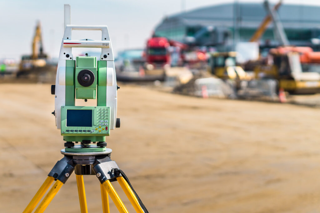 surveyor engineer with equipment (theodolite or total positioning station) on the construction site of the road or building with construction machinery background